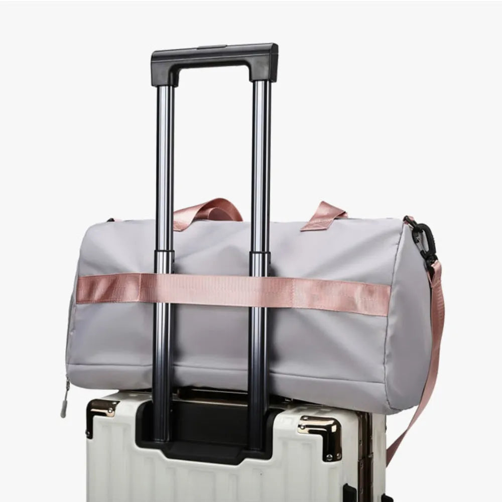 Gray duffel bag with pink strap detail and buckle, resting on a suitcase.