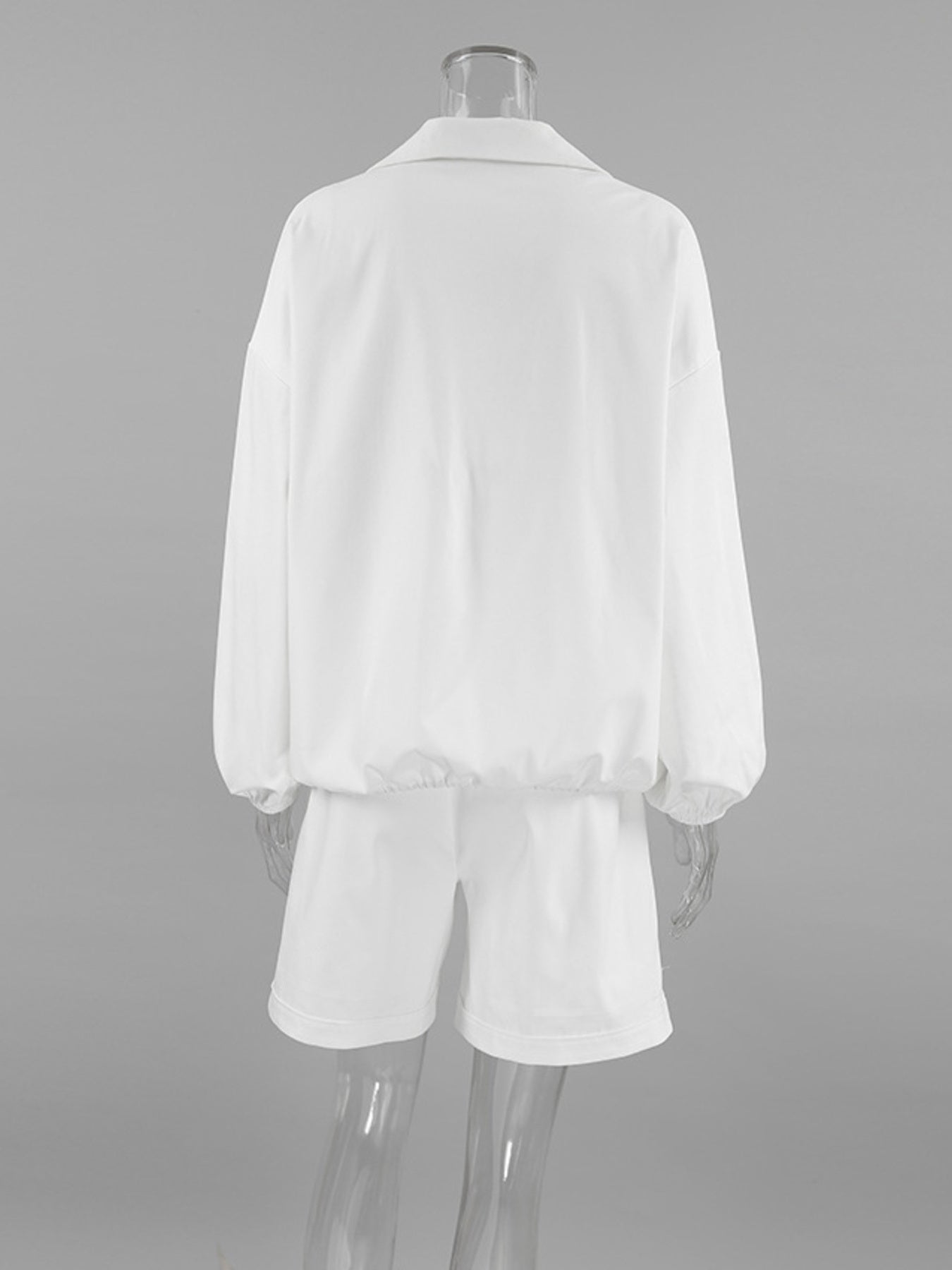 White two-piece set with collared long sleeve top and drawstring shorts, featuring snap details.