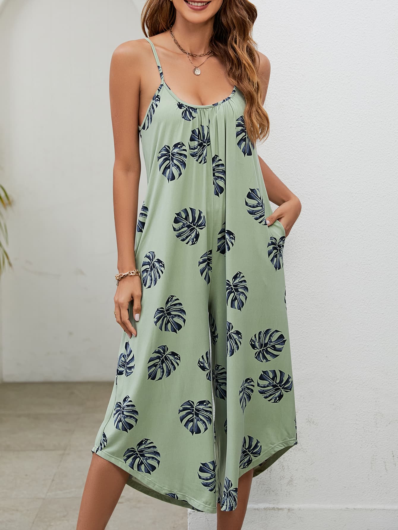 Sage green culotte jumpsuit with monstera print, gathered bust, and pockets.
