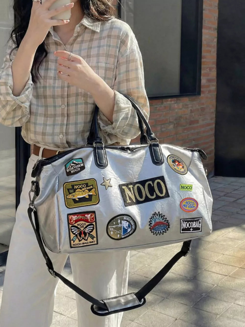 Metallic patchwork travel bag with textured finish and embroidered patches, featuring top handles and a crossbody strap.