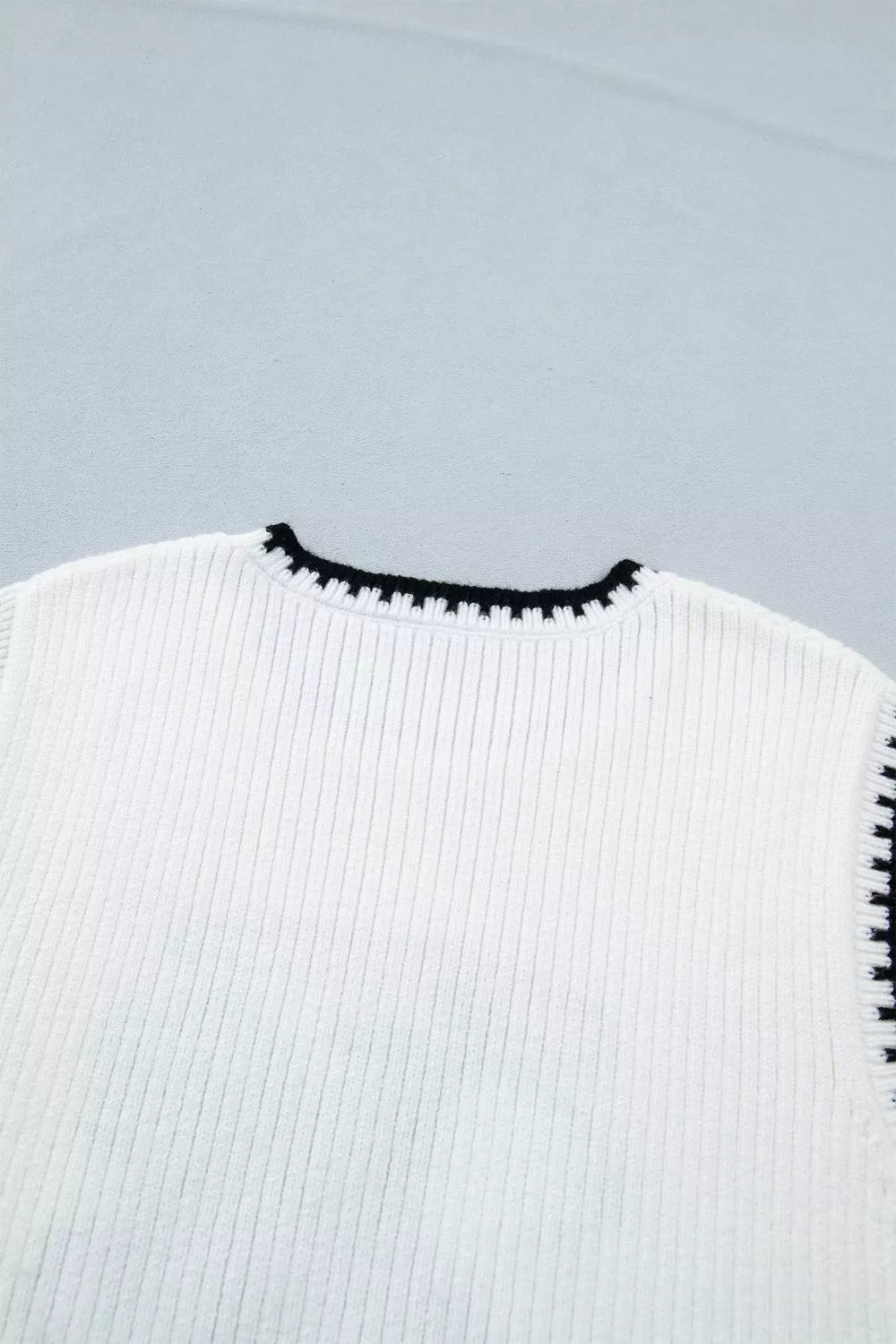 White ribbed sweater vest with black contrast trim neckline and armholes.