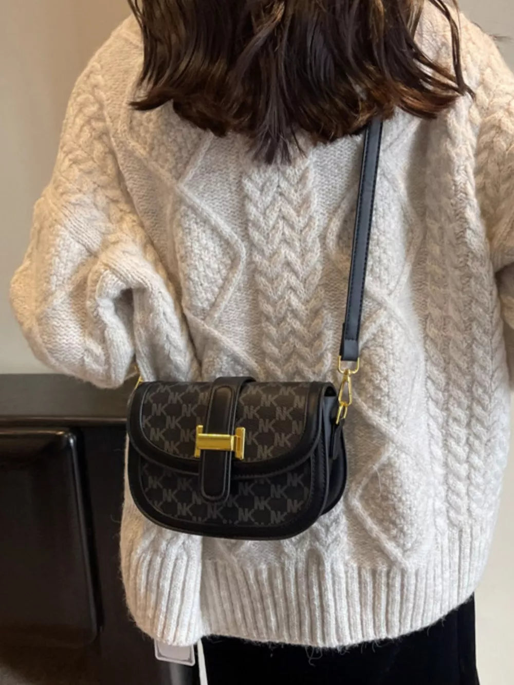 Black monogram flap crossbody bag with gold hardware and adjustable strap.