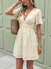 Chic textured mini dress with ruched waist, V-neck, and short sleeves.