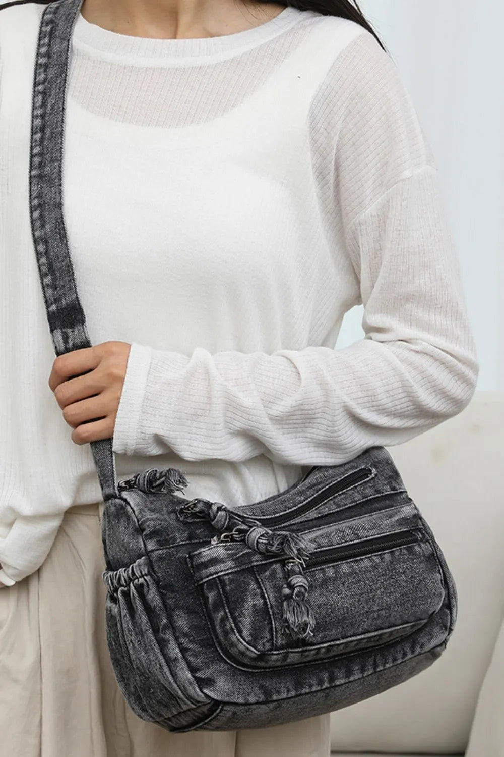 Acid wash denim crossbody bag in dark with tassel details and multiple pockets.