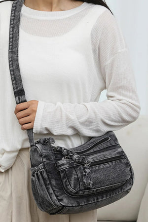 Acid wash denim crossbody bag in dark with tassel details and multiple pockets.
