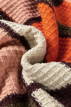 Waffle knit hoodie in colorblock orange, cream, and pink acrylic with textured patches.
