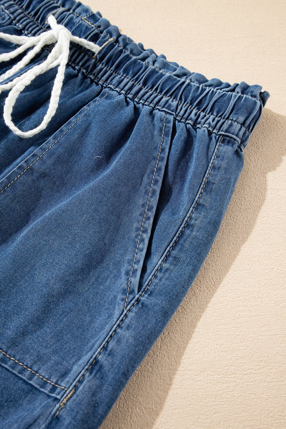 Navy denim drawstring shorts with elastic waist and white tie.