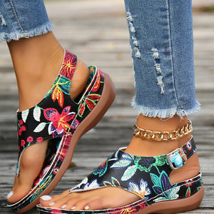 Black embroidered floral thong wedge sandals with adjustable ankle strap and gold chain detail.
