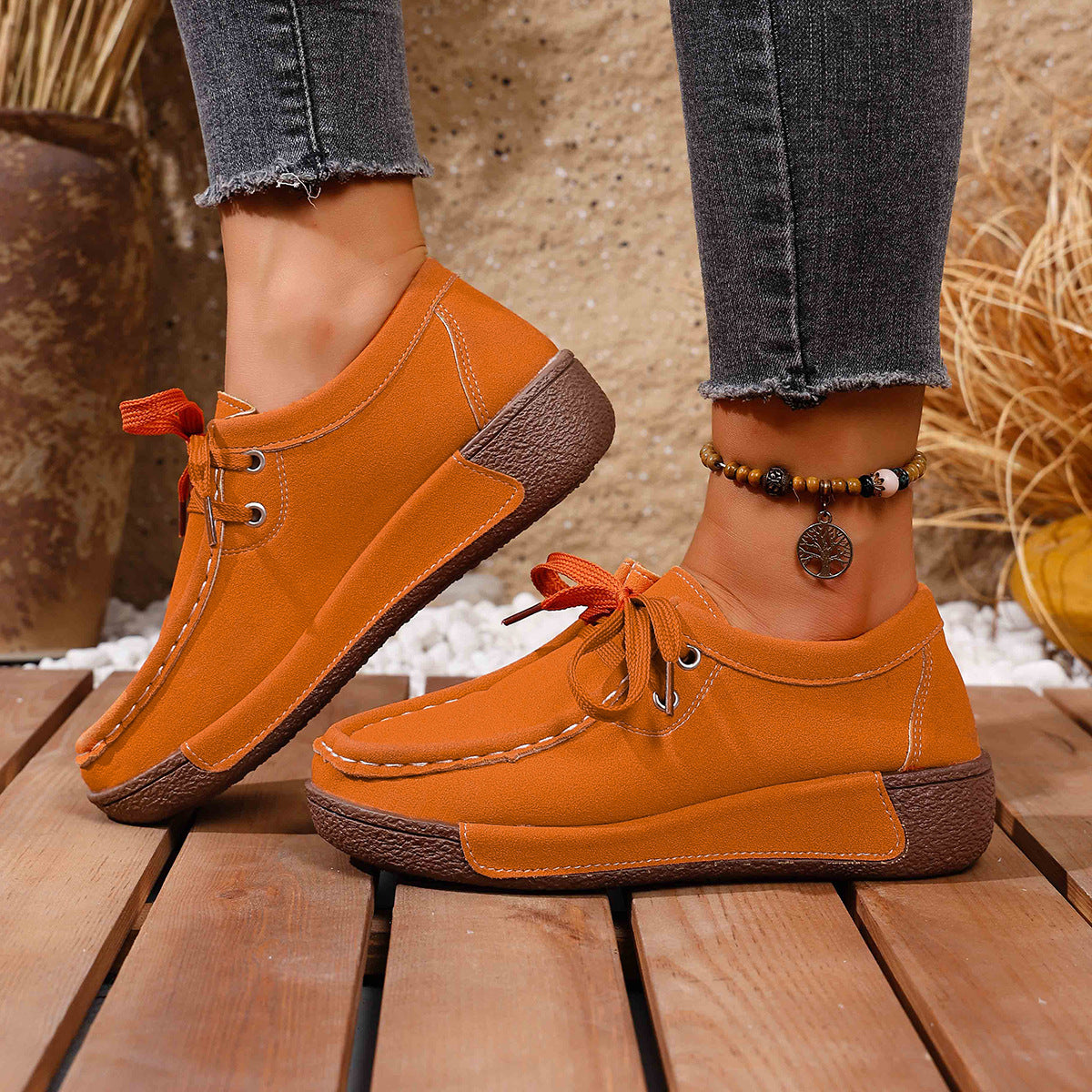 Orange lace-up moccasin style sneakers with brown soles and white stitching detail.