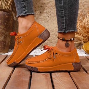 Orange lace-up moccasin style sneakers with brown soles and white stitching detail.