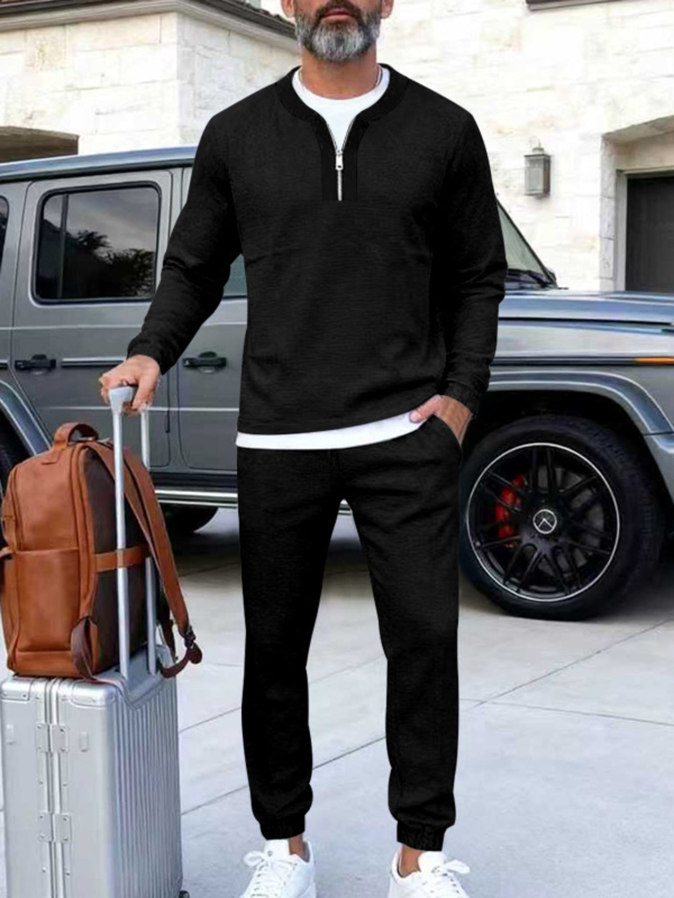 Black zippered top track pants set with a white undershirt, styled with a suitcase and backpack.