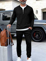 Black zippered top track pants set with a white undershirt, styled with a suitcase and backpack.