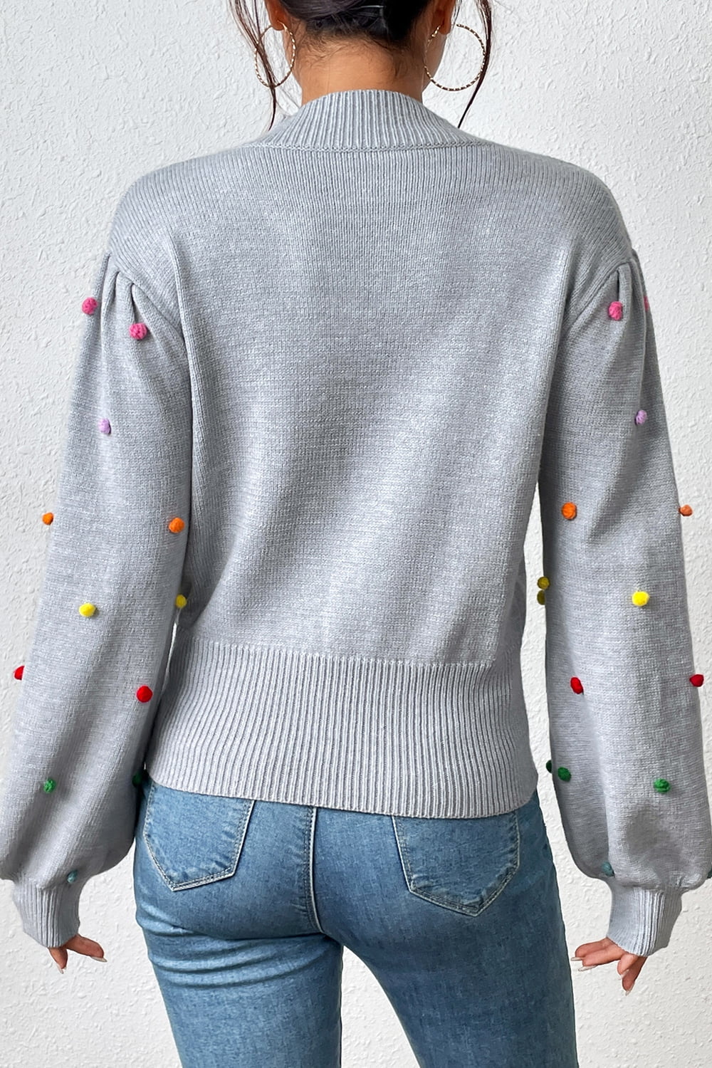 Light gray blouson sweater with colorful pom-pom embellishments on sleeves and shoulders.