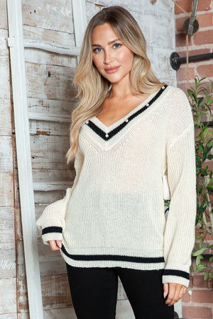 Cream ribbed knit V-neck sweater with pearl trim and black stripe details.