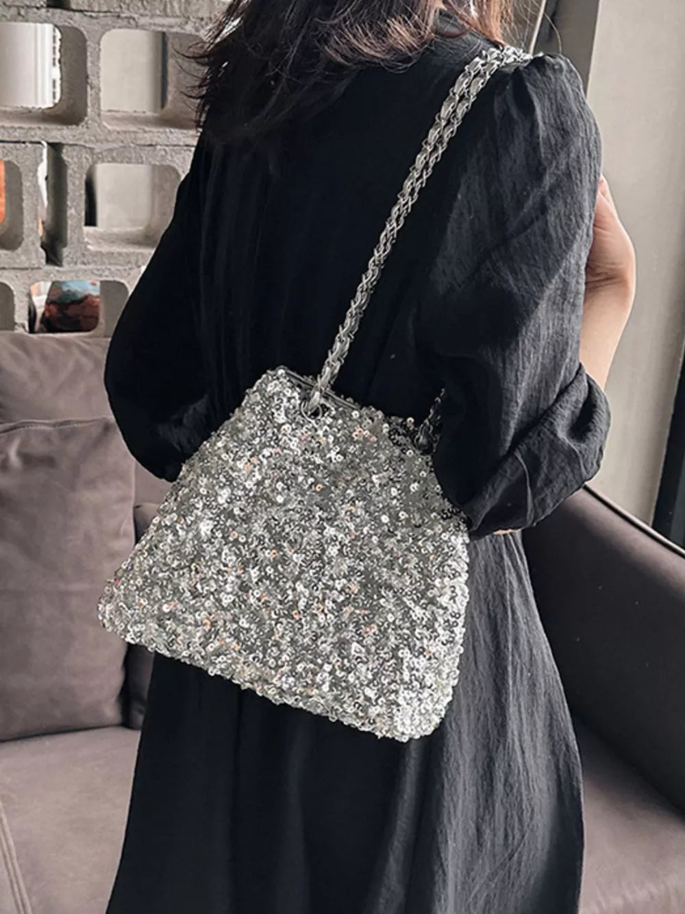 Silver sequin bucket bag with chain strap worn over the shoulder.
