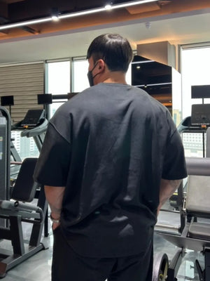 Black oversized t-shirt with short sleeves and a crew neck, worn by a man in a gym.