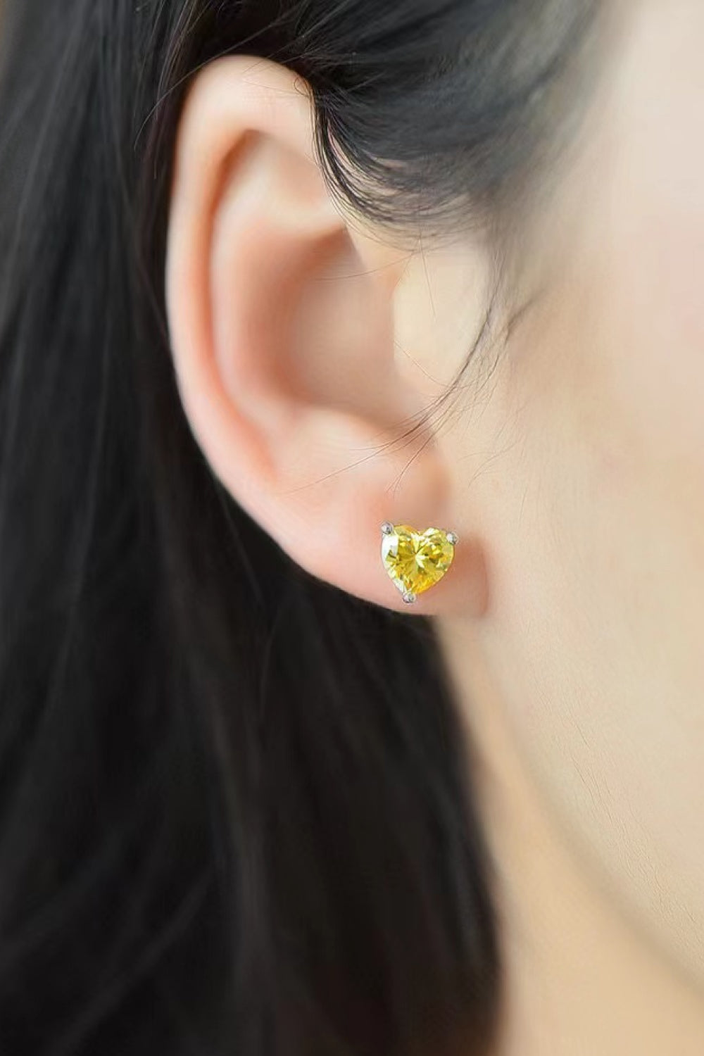 Yellow heart moissanite stud earrings on a woman's ear.