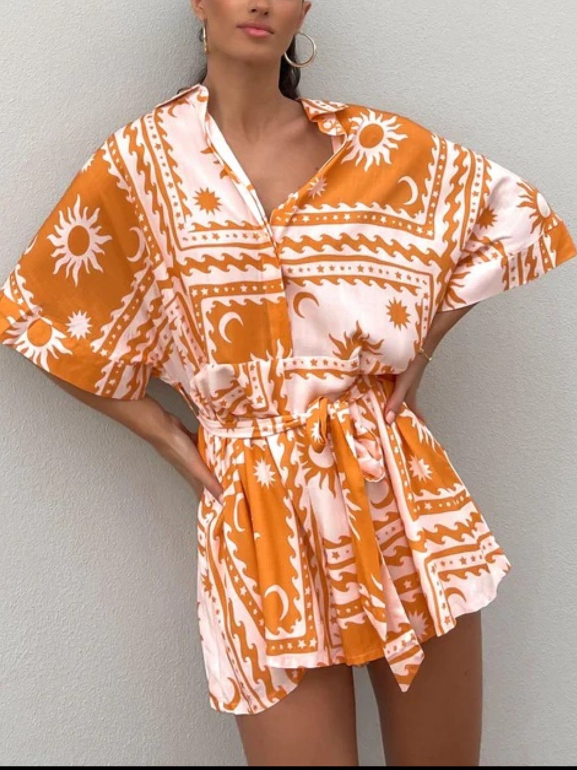 Celestial print wrap romper in orange and pink with short sleeves and a tie waist.