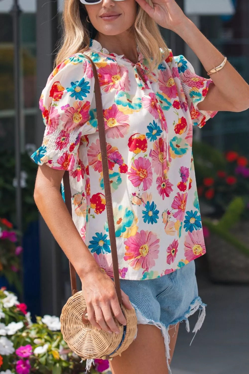 White cotton blend shirt with vibrant floral print, ruched short sleeves, and tie neck.