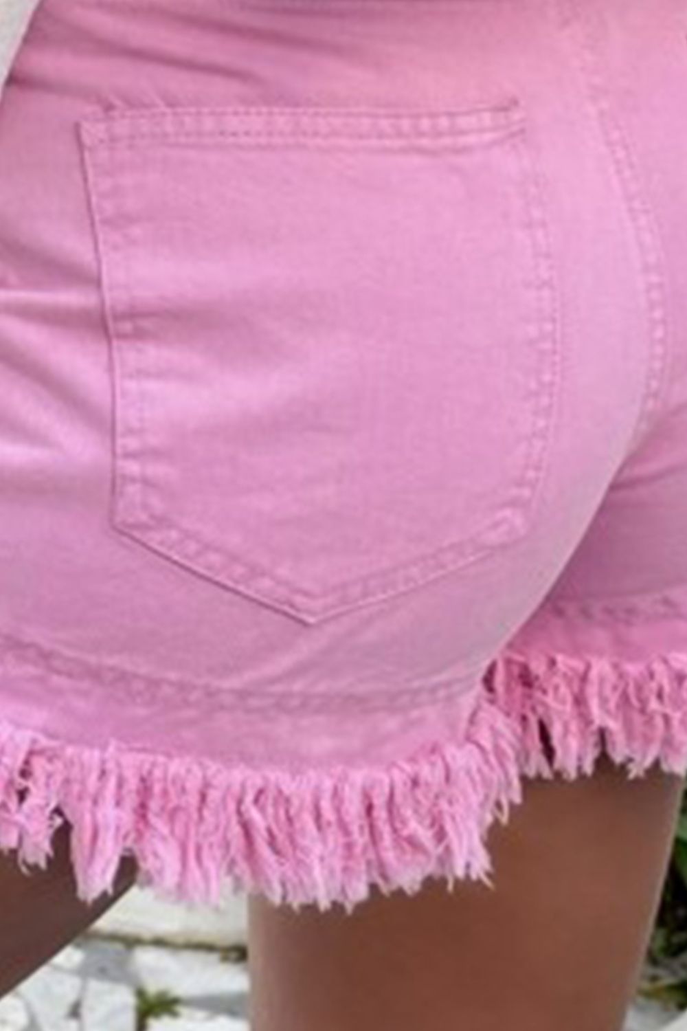 Pink denim shorts with high rise and frayed hem detail.