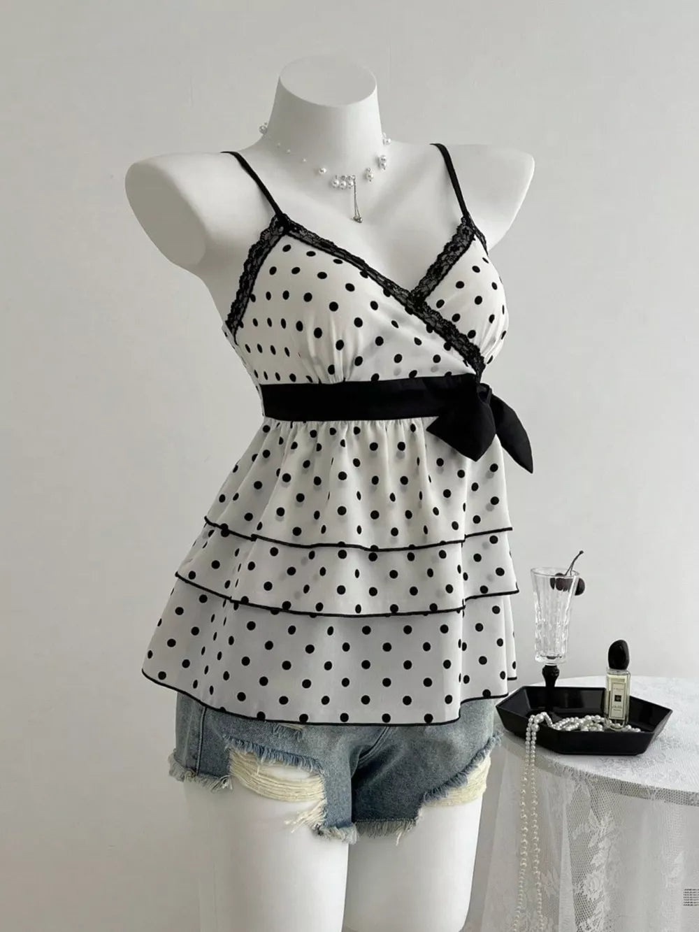 White polka dot camisole with black lace trim, tiered ruffles, and a black bow detail.