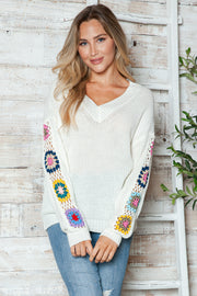 White knit sweater with colorful granny square sleeves and V-neck.