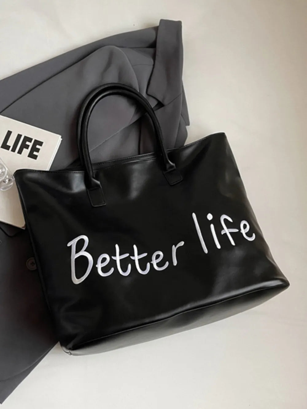 Black tote bag with white metallic "Better Life" graphic and double handles.
