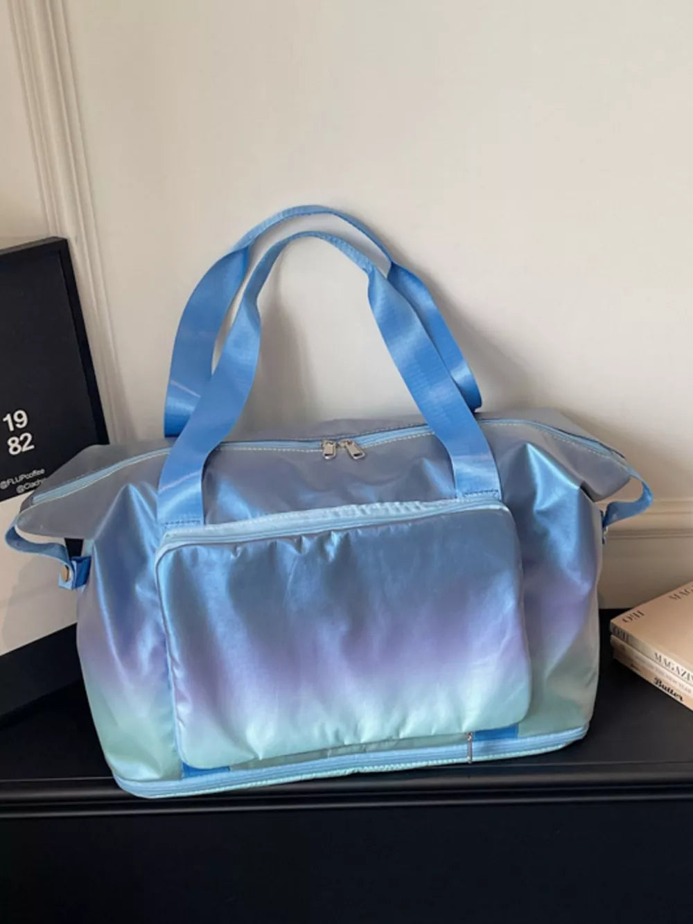 Iridescent gradient blue duffel bag with dual handles and front pocket.