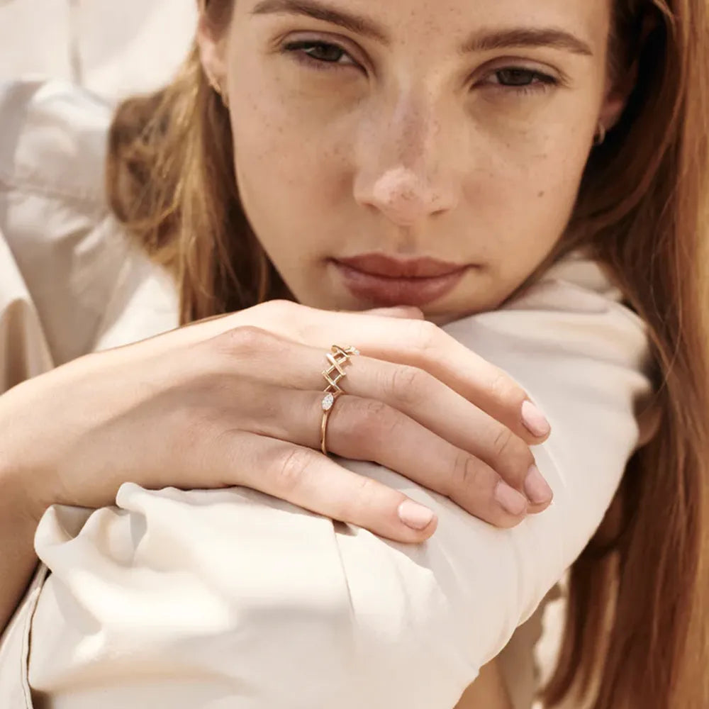 Gold openwork ring with geometric design and small diamonds on a woman's finger.