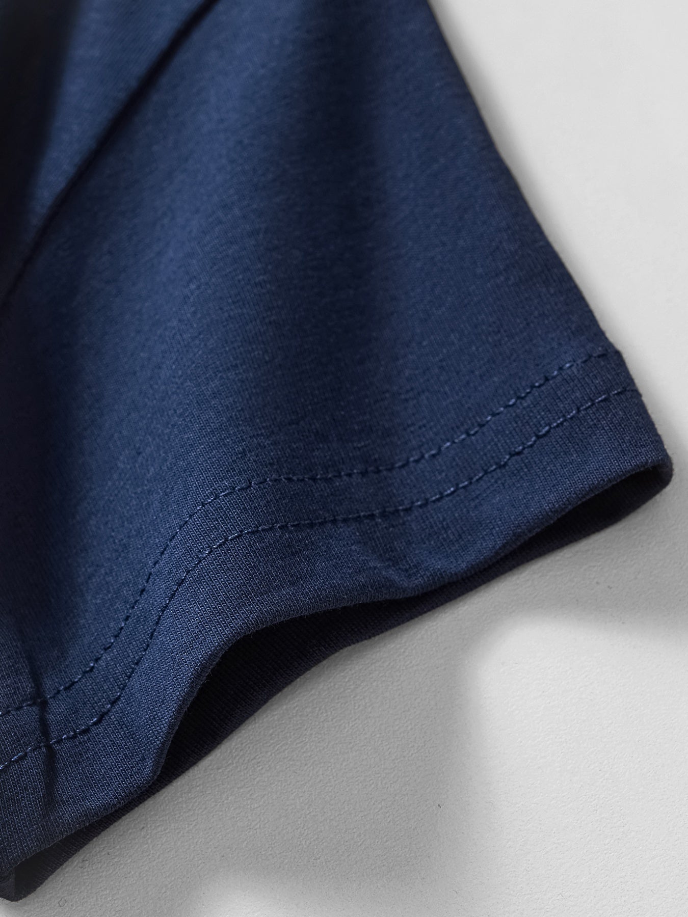 Navy blue cotton t-shirt sleeve hem with double-stitched detail.