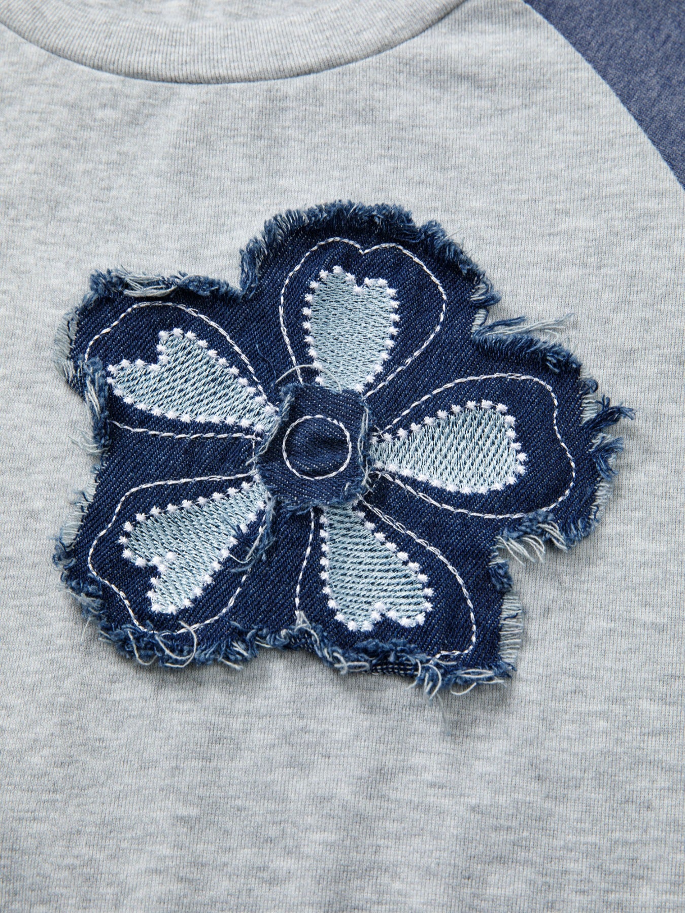 Raglan shirt with a distressed denim embroidered flower patch detail.