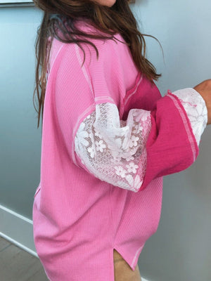 Pink waffle knit top with white lace paneled sleeves and cuffs.