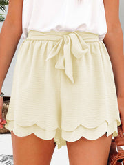 Ivory scalloped hemline tie-waist shorts with a textured fabric and a bow detail.