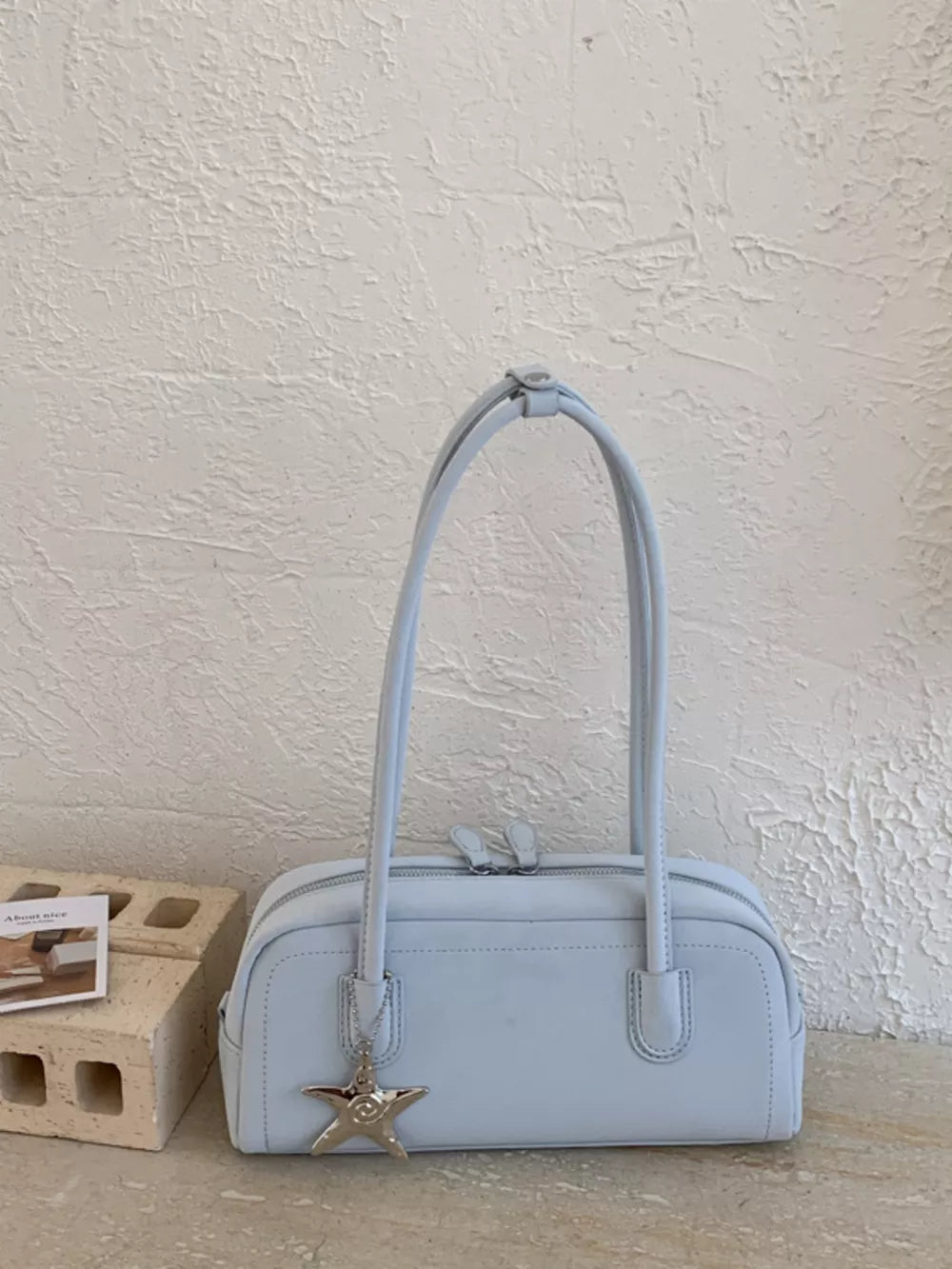 Light blue leather shoulder bag with star charm and double zipper.