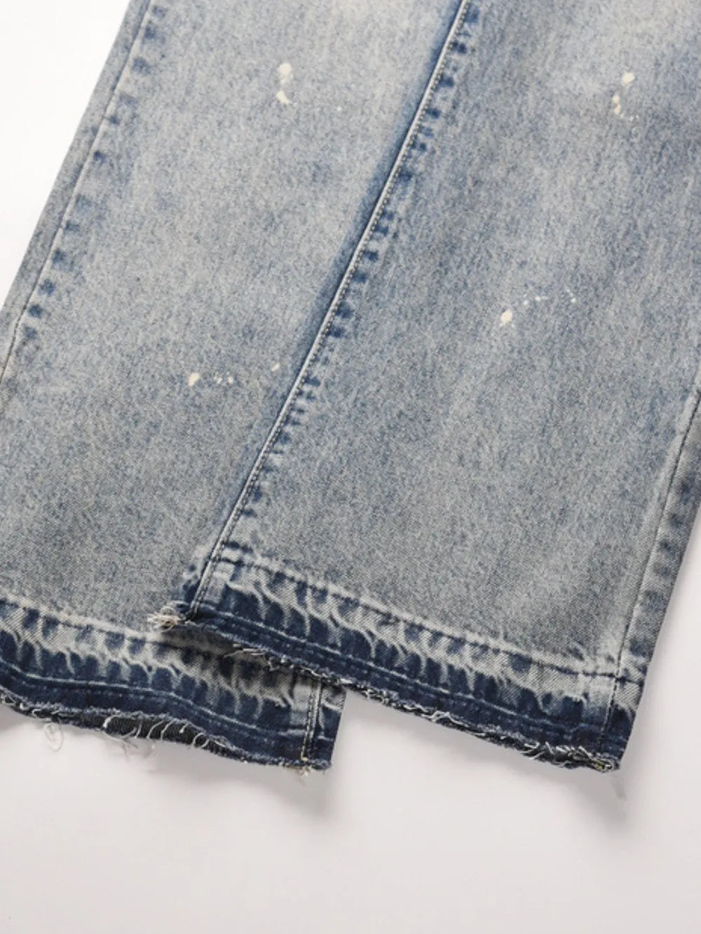 Distressed wash bootcut jeans with raw hem and paint splatters.