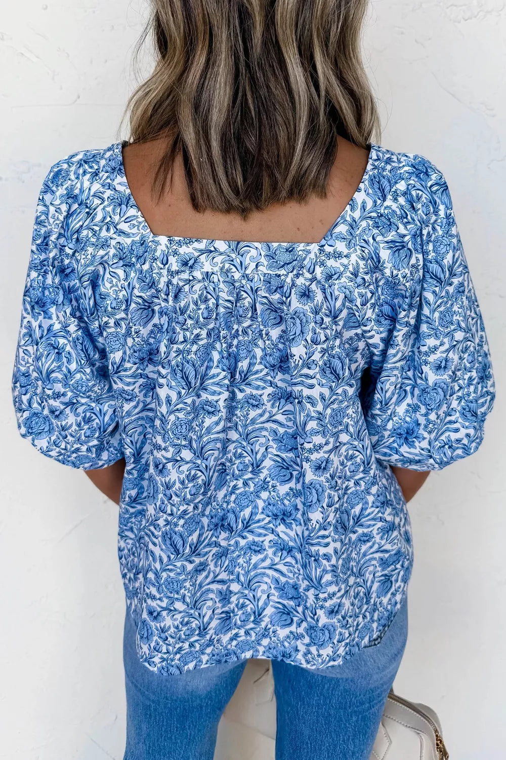 Floral pleated blouse with square neckline and puff sleeves in blue and white print.