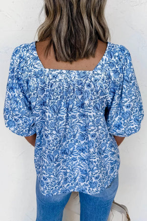 Floral pleated blouse with square neckline and puff sleeves in blue and white print.