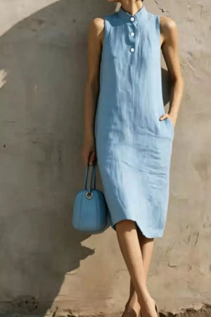 Light blue sleeveless midi dress with button accents and pockets, styled with a blue handbag.