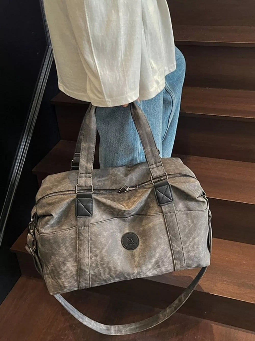 Distressed dark gray leather travel duffel bag with adjustable strap and top handles.