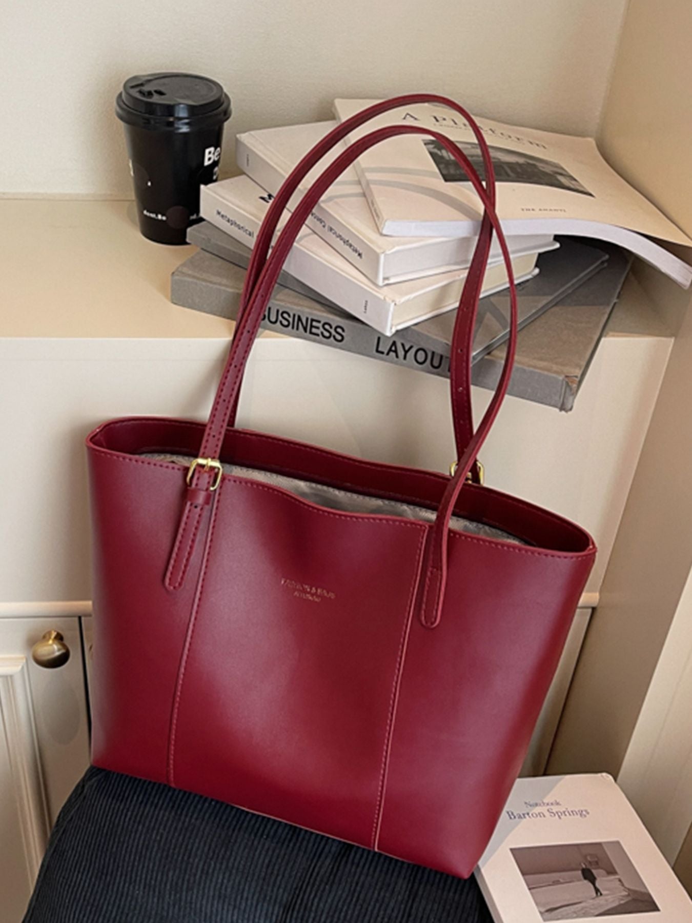 Sleek structured wine red pu leather tote bag with gold buckle detail and embossed logo.