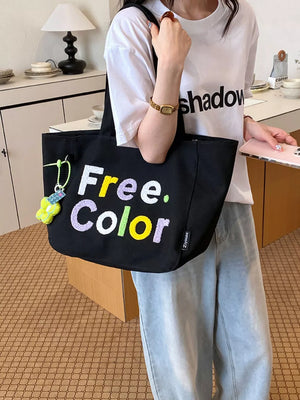 Black canvas shoulder bag with embroidered "Free. Color" text and a charm.