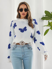 White distressed knit cropped sweater with blue butterfly print and frayed hem.