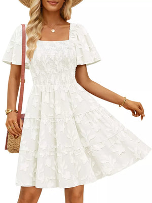 White smocked mini dress with tiered skirt, flutter sleeves, and floral texture.