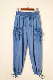 Light wash denim maternity cargo jeans with drawstring waist, cinched ankles, and tie-detail pockets.