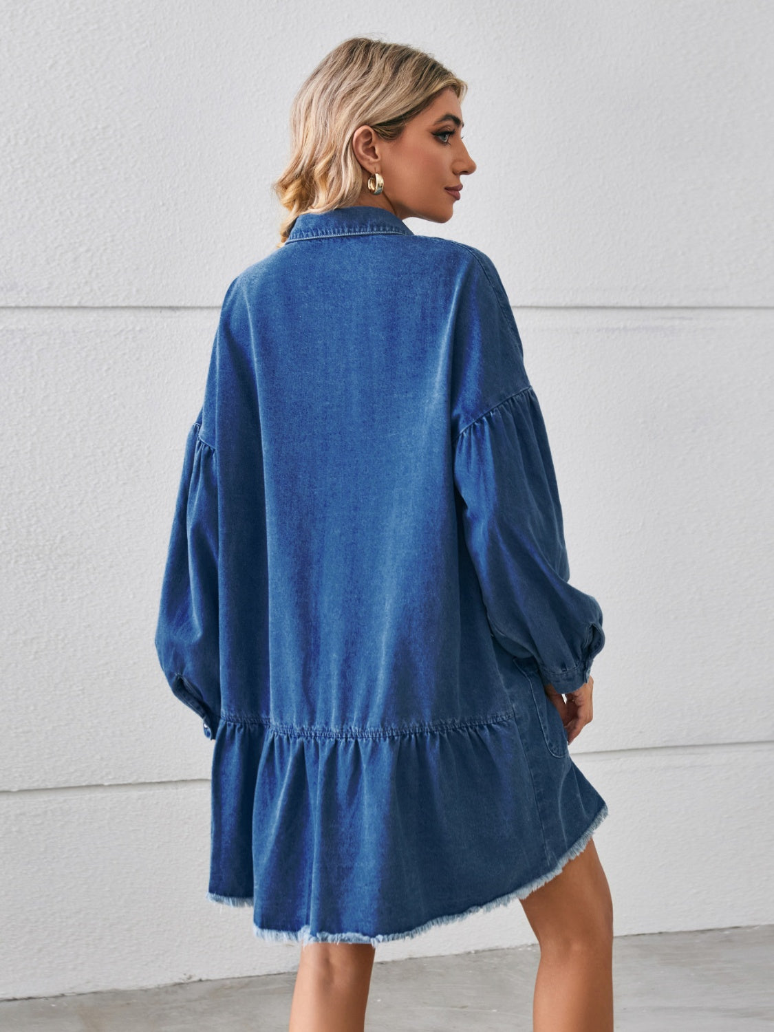 Dark blue denim shirtdress with voluminous sleeves, button front, tiered ruffled hem, and frayed edges.