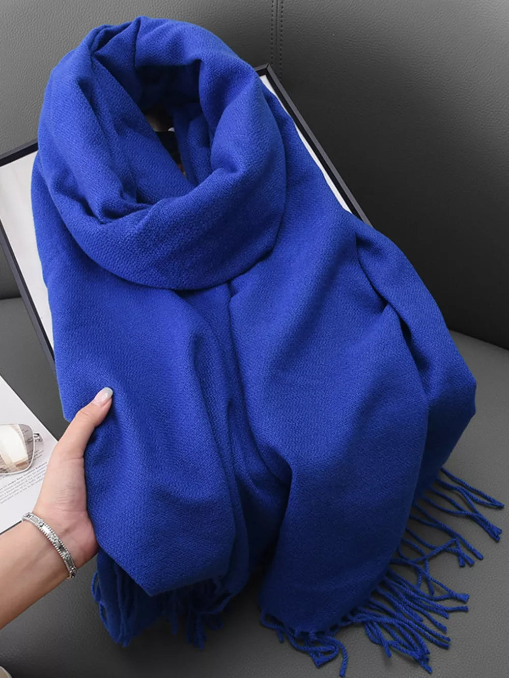 Blue fringed scarf with a textured weave, styled loosely.
