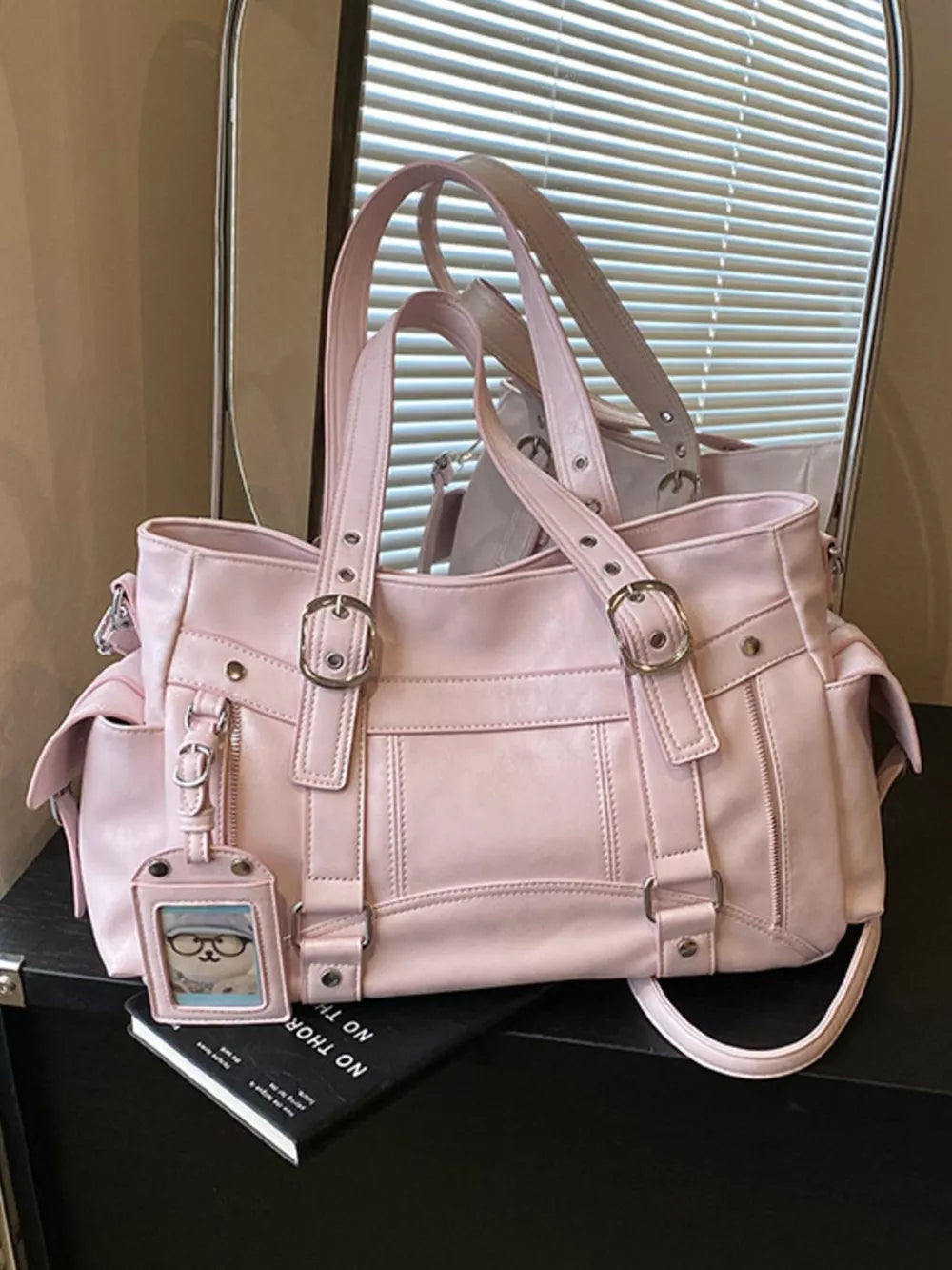 Pink shoulder bag with buckle details and a cute charm.