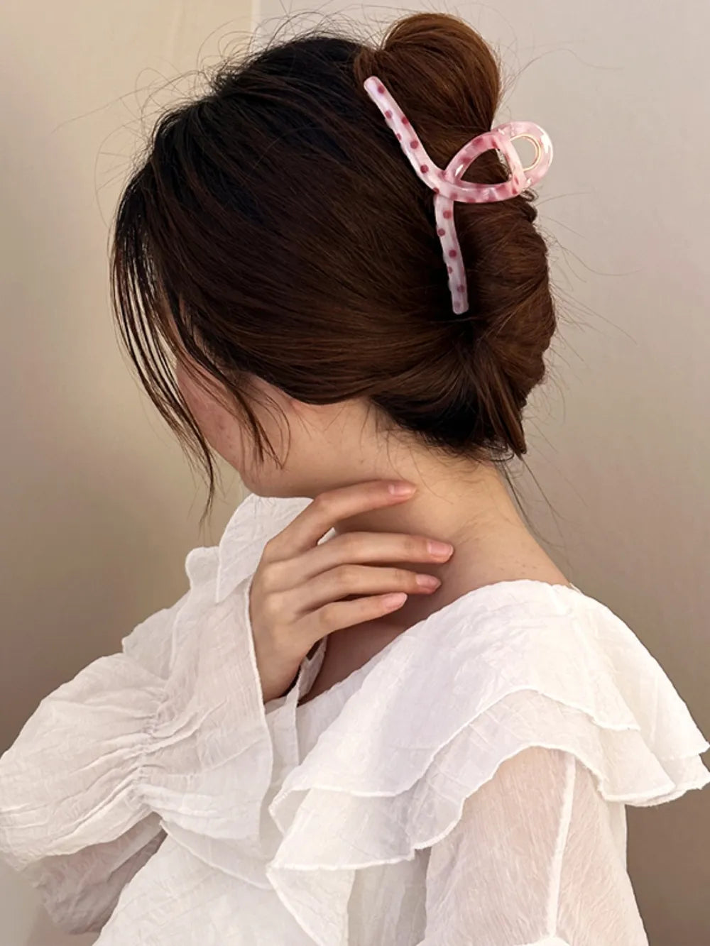 Polka dot claw hair clip in pink with a knot design, holding up brown hair.
