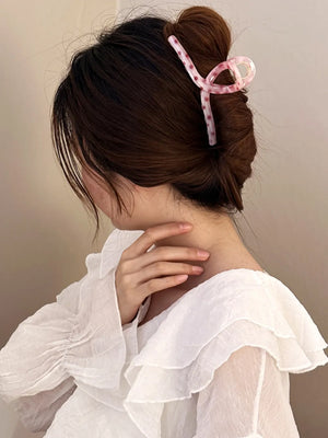 Polka dot claw hair clip in pink with a knot design, holding up brown hair.