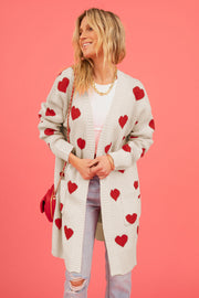Cream longline knit cardigan with red heart motif, pockets, and open front.